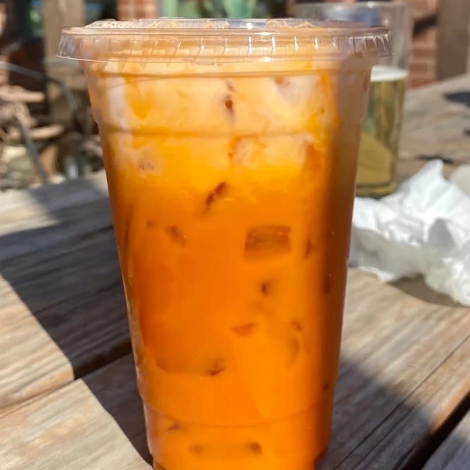 Iced Thai tea with a creamy top layer and ice, on a wooden table outdoors.